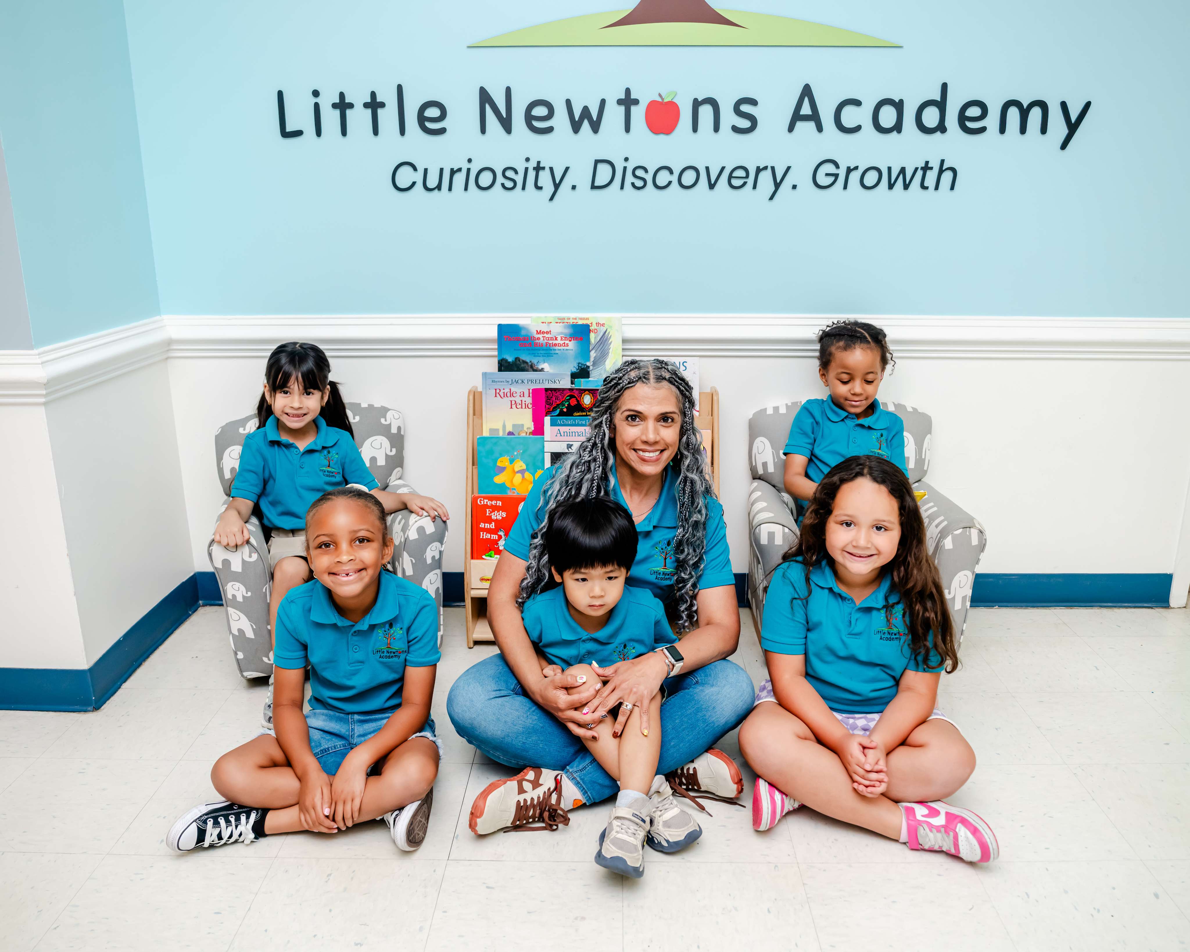 A teacher and smiling children beneath the Little Newtons Academy sign